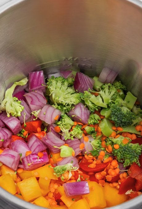 Verduras picadas dentro del jarro de acero de MioMat Pro: cebolla morada, brócoli, pimentón y lentejas
